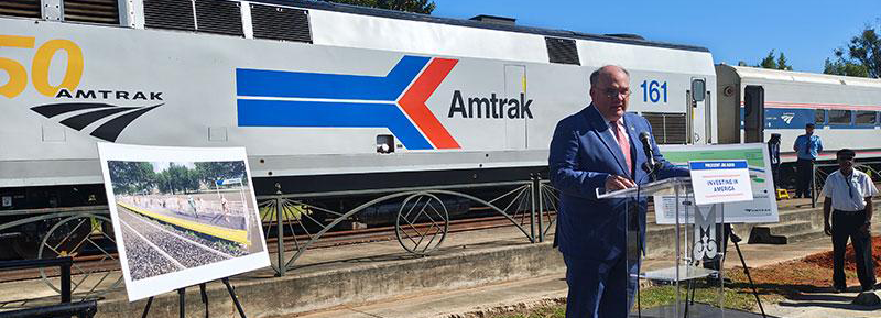 A man gives a speech in front of an Amtrak train.