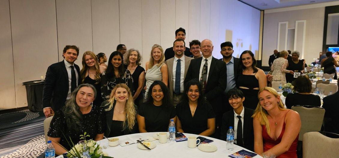Left, front: Susan Cheng, and next to her Isabella Parise with the Office of Public Health Practice, surrounded by students at a table at an event, smiling for the camera