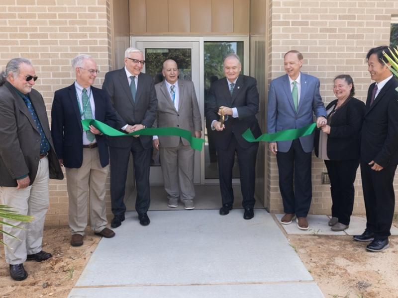 Eight people cutting green ribbon at building official opening.