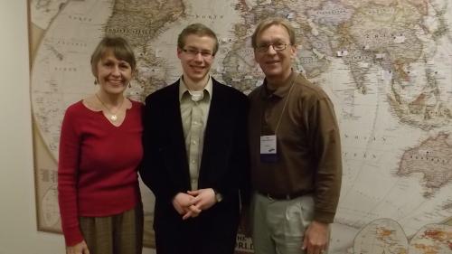 Charles Monzelun, his wife, and his son pose against a vintage world map.