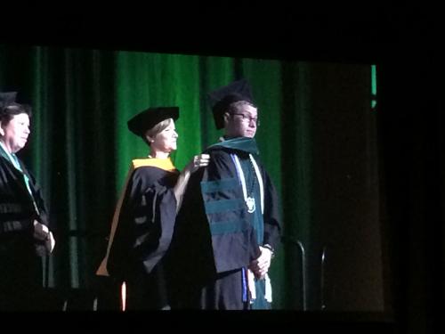 Professor places academic hood on a Charles Monzelun during a ceremony.