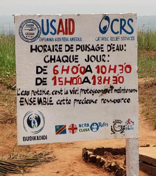 Sign with water hours in French, sponsored by USAID and CRS