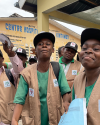 Group of young Black men smiling, wearing vests with organization badges, standing outside of a Health Centre in Kintambo